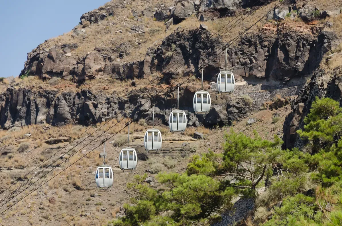 Fira cable car cabins climbing the caldera cliff above the Old Port in Santorini