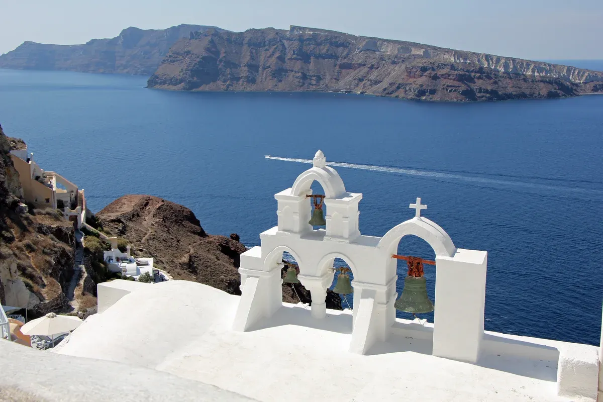 Whitewashed bell tower in Oia with the caldera and Thirasia behind it on a Santorini catamaran cruise