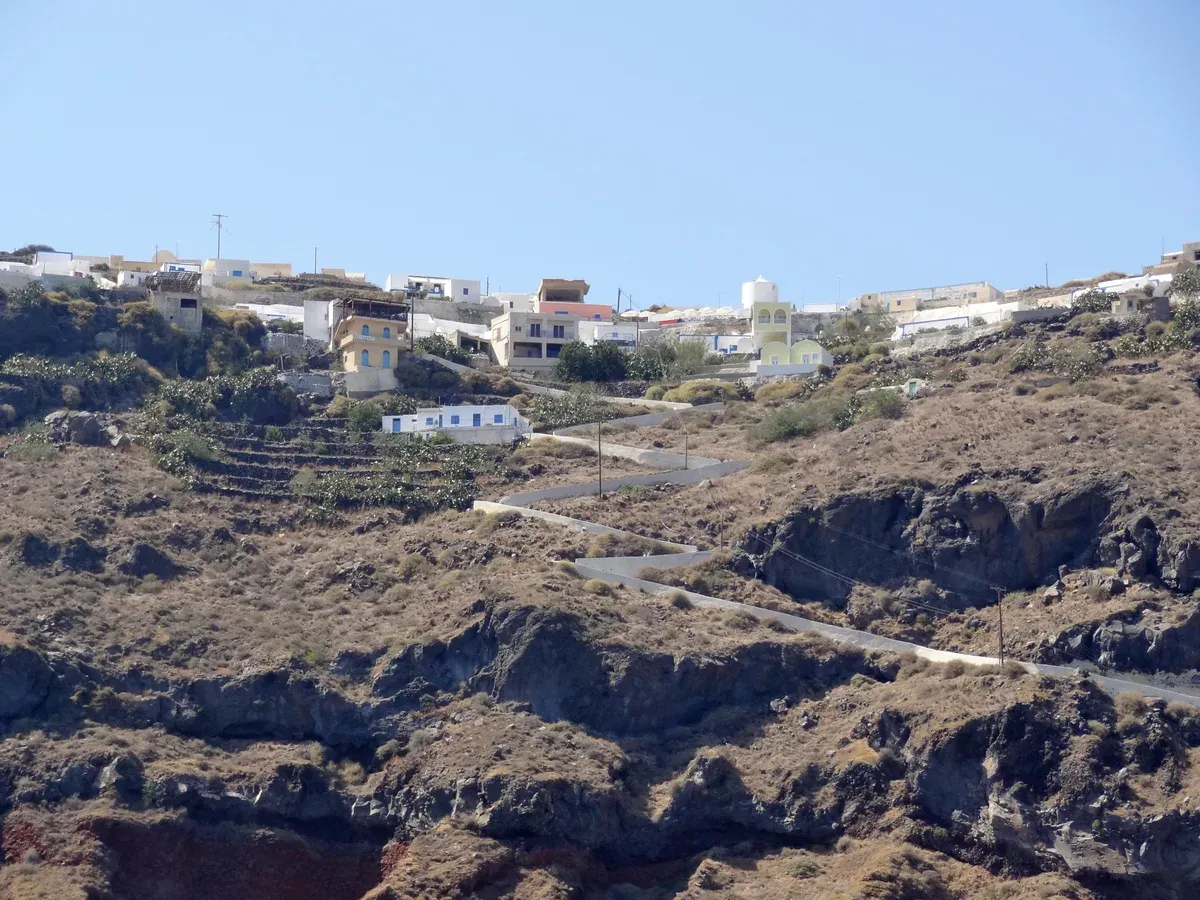 Houses of Manolas above the cliff road on Thirasia seen from the water on a Santorini catamaran cruise